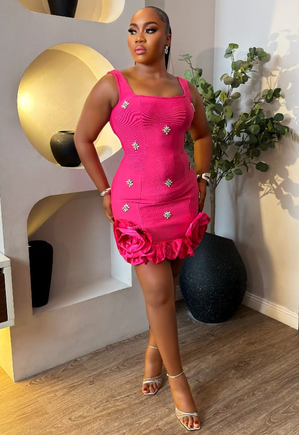 Light pink Blush Elowyn Dress by STERA FASHION displayed on a hanger with floral background.